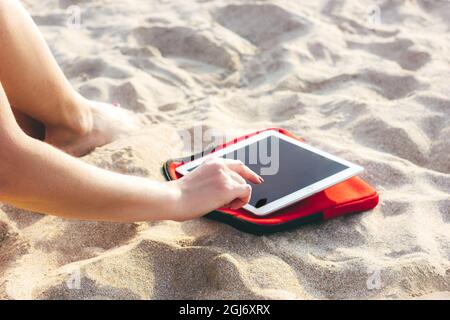 Giovane donna sportiva che usa un tablet sulla spiaggia per guardare i corsi di fitness. Comunicazione wireless e Internet per uno stile di vita attivo, yoga e attività fisica Foto Stock