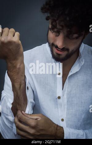 ritratto di un giovane uomo con barba e capelli ricci che regola le maniche della sua camicia bianca mentre si vestiva Foto Stock