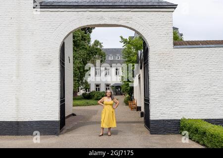 Ingresso ad arco tra due pareti di mattoni bianchi con una donna matura sorridente in abito giallo con sospensori, guardando la macchina fotografica, edificio con vento Foto Stock