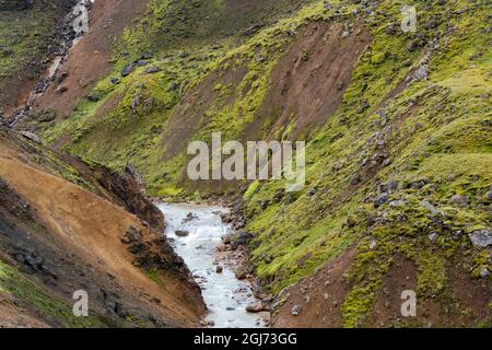 Islanda, Highlands meridionali, Monti Kerlingarfjoll. Un ruscello glaciale taglia la pietra rossa della rhyolite vulcanica che è coperta di grée brillante Foto Stock