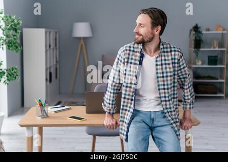 Foto di dolce sognante ragazzo maturo vestito a scacchi camicia sorridente tavolo da seduta al coperto ufficio appartamento Foto Stock