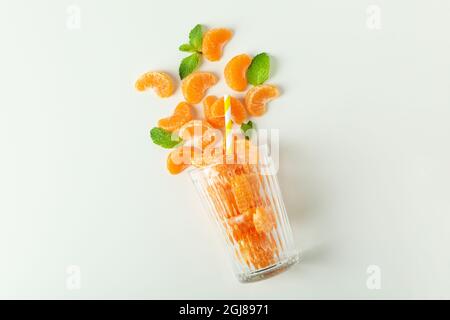 Concetto di produzione di succo di mandarino con bicchiere con mandarini su sfondo bianco. Foto Stock