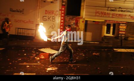 ISTANBUL 2014-05-22 Un uomo mascherato lancia un cocktail Molotov. La polizia turca di sommosse usa un cannone ad acqua per disperdere i manifestanti durante una protesta contro il governo, a Istanbul, Turchia, il 22 maggio 2014. Un gruppo di manifestanti si è scontrato con la polizia di sommosse turca durante una protesta contro il governo turco che vede responsabile dell'esplosione della miniera di Soma. Secondo quanto riferito, l'AKP del primo ministro Recep Tayyip Erdogan ha respinto in aprile una mozione del Partito popolare Repubblicano (CHP) di centro-sinistra per rivedere la sicurezza nella miniera di Soma. Il peggiore disastro minerario della storia del paese ha lasciato almeno 301 lavoratori d Foto Stock