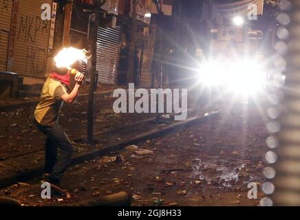 ISTANBUL 2014-05-22 Un uomo mascherato lancia un cocktail Molotov. La polizia turca di sommosse usa un cannone ad acqua per disperdere i manifestanti durante una protesta contro il governo, a Istanbul, Turchia, il 22 maggio 2014. Un gruppo di manifestanti si è scontrato con la polizia di sommosse turca durante una protesta contro il governo turco che vede responsabile dell'esplosione della miniera di Soma. Secondo quanto riferito, l'AKP del primo ministro Recep Tayyip Erdogan ha respinto in aprile una mozione del Partito popolare Repubblicano (CHP) di centro-sinistra per rivedere la sicurezza nella miniera di Soma. Il peggiore disastro minerario della storia del paese ha lasciato almeno 301 lavoratori d Foto Stock