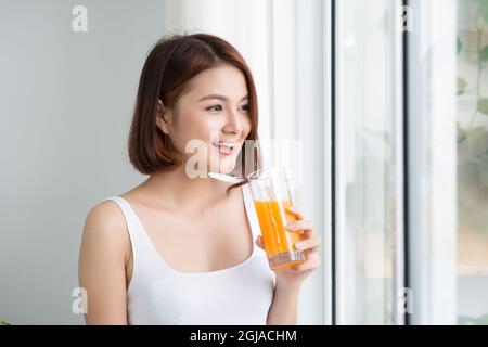 Bella giovane donna asiatica in camera luminosa che beve succo d'arancia Foto Stock