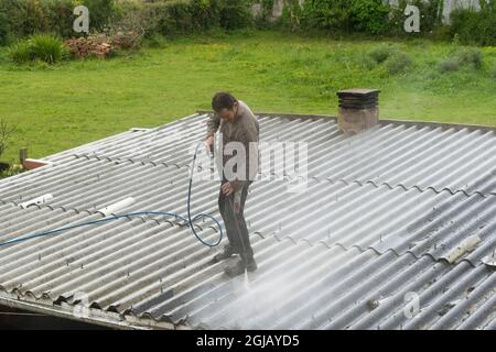 Uomo che pulisce un tetto con una pistola ad acqua pressurizzata Foto Stock