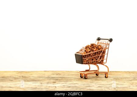 I chicchi di caffè vengono versati con uno scivolo in un carrello, poggiando su una superficie di legno contro uno sfondo beige chiaro. Primo piano, spazio di copia. Foto Stock