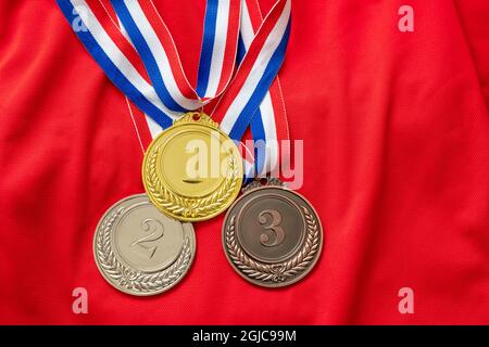 Medaglie, oro, argento e bronzo. Vincitori, trofeo premio atleti podio su sfondo rosso camicia. Primo, secondo e terzo posto premio appeso Foto Stock