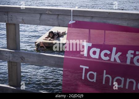 Le giovani donne godono di una giornata estiva soleggiata al lago Malaren come un segno di allontanamento sociale appeso su una recinzione, in mezzo alla malattia del coronavirus (COVID-19), a Stoccolma, Svezia, il 31 luglio 2020. Poto: Naina Helen Jama / TT / code 11880 *** SWEDEN OUT *** Foto Stock