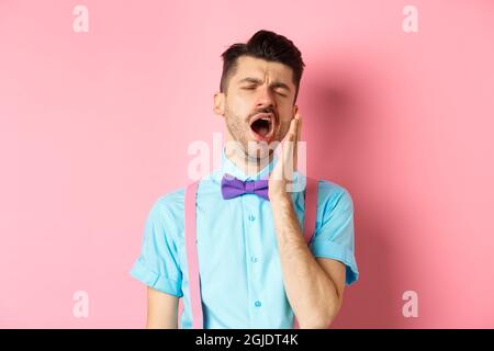 Immagine di un ragazzo stanco con bretelle a bocca aperta e occhi chiusi, in piedi sonnolenti, sensazione di stanchezza, in piedi su sfondo rosa Foto Stock