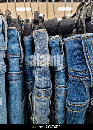 Primo piano di una fila di jeans blu denim appesi su appendiabiti di plastica in negozio Foto Stock