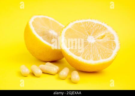 Capsule vitaminiche. Pillole di vitamina C e limone giallo su sfondo giallo. Foto Stock