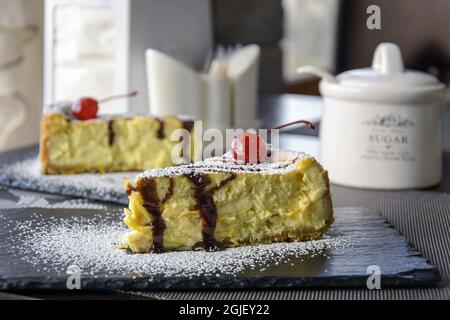 Due pezzi di cheesecake con ciliegie su tavolini di pietra nera al tavolo in un caffè. Primo piano. Messa a fuoco selettiva. Foto Stock