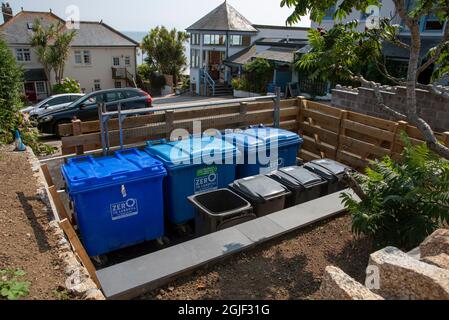 Cornovaglia, Inghilterra, Regno Unito. 2021. Contenitori di riciclaggio in plastica blu e nera in un'area recintata vicino all'alloggiamento. Foto Stock