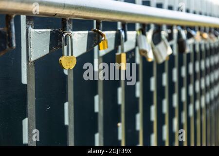 Lucchetto a forma di cuore appiccato sulle rotaie tra gli altri lucchetti variegati Foto Stock