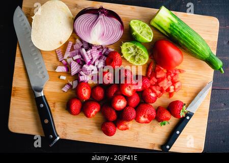 Preparare frutta e verdura su un tagliere di bambù: Frutta e verdura tritate con un coltello santoku e un coltello da parare su sfondo di legno Foto Stock