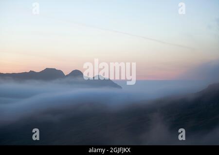 I Langdale Pikes si innalzano sopra un'inversione di nuvole, all'alba nel Lake District inglese Foto Stock