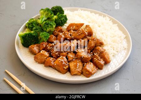 Pollo Teriyaki fatto in casa con riso e broccoli su un piatto su sfondo grigio, vista laterale. Foto Stock