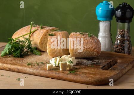 Rotolo di formaggio appena sfornato. Rotolo bianco e formaggio tagliato a dadini. Sale e pepe in matracci trapuntati. Pane affettato sul bordo. Foto Stock