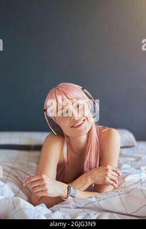 Ritratto di bel modello con capelli rosa che ascoltano musica sul comodo letto di casa Foto Stock