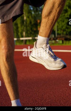 Primo piano giovane atleta uomo runner prepararsi a correre facendo esercizi di riscaldamento e stretching per i muscoli delle gambe prima di allenarsi all'esterno per maratona su campo atletico all'alba Foto Stock