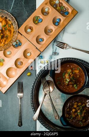 Giocare gioco da tavolo mancala mentre si mangia cibo indiano tra cui pollo tikka e pindi chana masala così come aloo matar Foto Stock