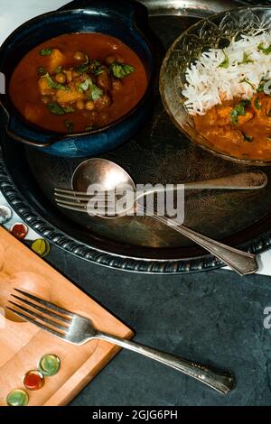 Giocare gioco da tavolo mancala mentre si mangia cibo indiano tra cui pollo tikka e pindi chana masala così come aloo matar Foto Stock