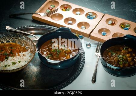 Giocare gioco da tavolo mancala mentre si mangia cibo indiano tra cui pollo tikka e pindi chana masala così come aloo matar Foto Stock