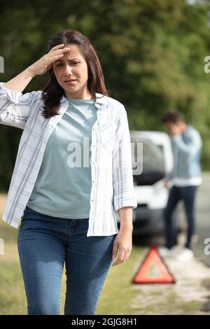 donna sconvolto vicino triangolo di avvertimento e auto rotta Foto Stock
