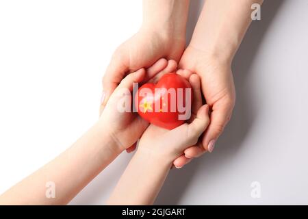 Mani di donna e bambino con piccolo cuore nei colori della bandiera cinese su sfondo bianco Foto Stock