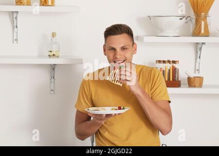 Bel giovane uomo che mangia gustosa quesadilla a casa Foto Stock
