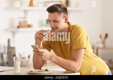 Bel giovane uomo che mangia gustosa quesadilla a casa Foto Stock