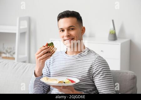Bel giovane uomo che mangia gustosa quesadilla a casa Foto Stock