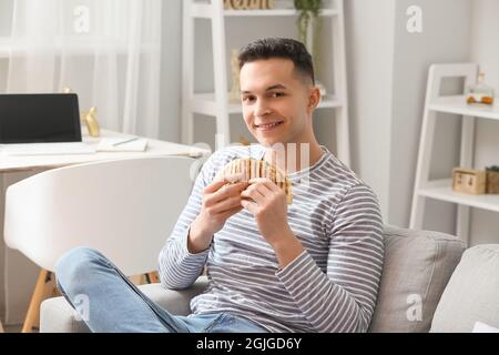 Bel giovane uomo che mangia gustosa quesadilla a casa Foto Stock