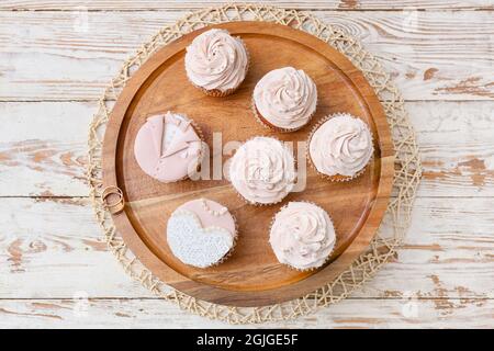 Dessert stand con gustosi cupcakes e anelli di nozze su sfondo di legno Foto Stock