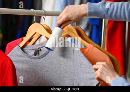 Donna che pulisce la t-shirt con il rullo di pelucchi in camera Foto Stock