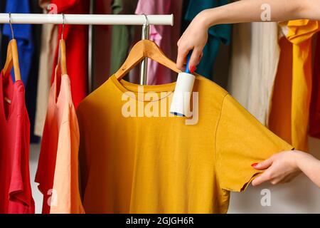 Donna che pulisce la t-shirt con il rullo di pelucchi in camera Foto Stock