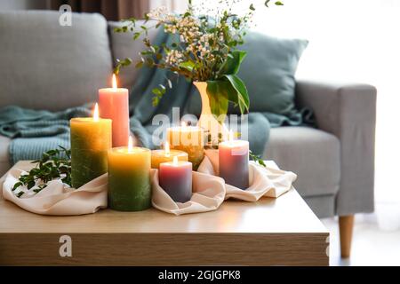 Candele brucianti e rami di pianta su tavola di legno in camera Foto Stock