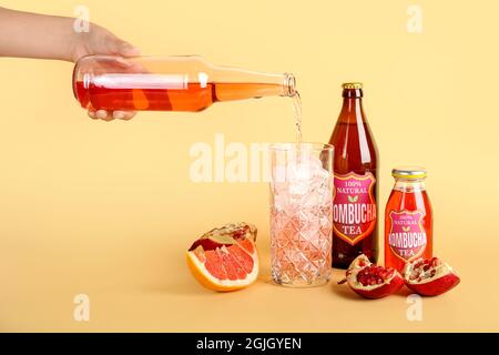 Donna che versa il gustoso tè kombucha dalla bottiglia in vetro su sfondo colorato Foto Stock