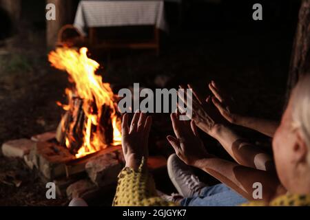 Le donne mature scaldano le mani vicino al fuoco la sera d'estate Foto Stock