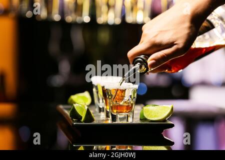 Barista che versa la gustosa tequila in bicchieri al tavolo al bar Foto Stock