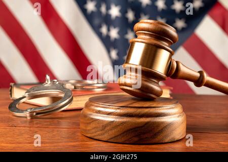 Un gavel e blocco di legno riposano in cima alla scrivania di un giudice con un libro legale e bandiera americana sfondo. Foto Stock