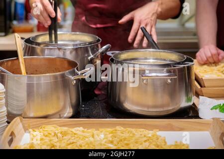 Lo chef prepara la pasta in grandi padelle metalliche. Le mani maschili estrarano la pasta dalla padella con le pinze. Primo piano. Foto Stock