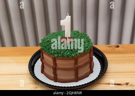 Torta al cioccolato decorata. Un anno di candela bianca su torta decorata in tema country su un tavolo di legno chiaro. Foto Stock