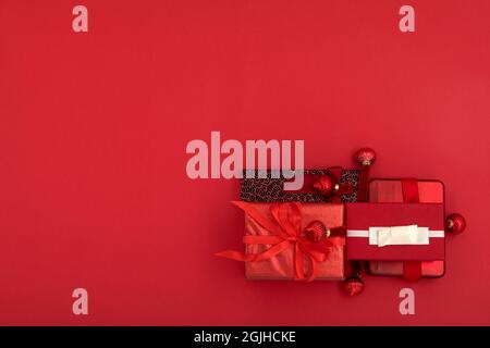 Vista dall'alto composizione di vari regali natalizi avvolta in carta con nastri e sfere decorative poste su una superficie rossa brillante con spazio vuoto Foto Stock