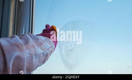 Primo piano delle mani nei guanti pulizia della finestra con uno straccio sullo sfondo del cielo limpido Foto Stock