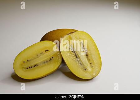 Primo piano di un Kiwifruit d'oro o di una bacca cinese (Actinidia chinensis) tagliata longitudinalmente e di una bacca intera su sfondo bianco Foto Stock