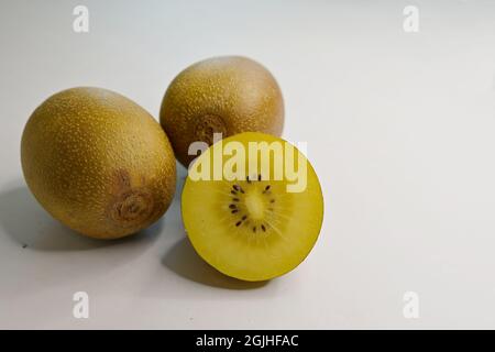 Primo piano di un Golden Kiwifruit tagliato o uva spina cinese (Actinidia chinensis) e 2 bacche intere su sfondo bianco Foto Stock