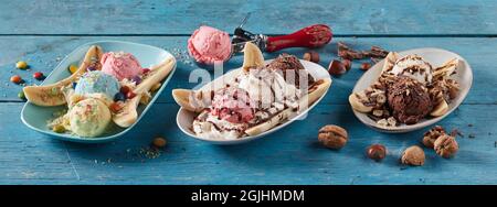 Alto angolo di dolci assortiti alla banana con palle di gelato serviti su piatti in fila su sfondo di legno blu Foto Stock