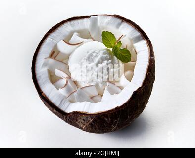 Da sopra di gelato freddo scoop decorato con foglie di menta servito in guscio di cocco su sfondo bianco Foto Stock